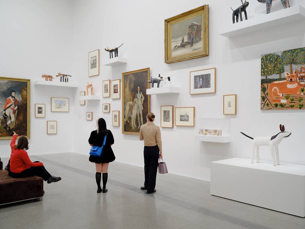Two art exhibition visitors peer at a wall of paintings at NGV Australia in Melbourne's Fed Square.