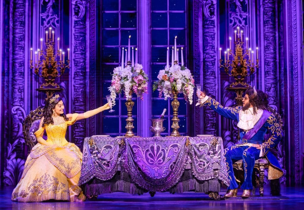 Belle in a yellow ballgown and Beast in a blue suit raising their glasses in Beauty and the Beast