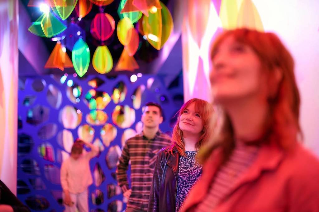 people experiencing the Bring it to the Runway, Runway room in the Joy exhibition at the Immigration Museum, they're looking up at colourful jewels dangling from the ceiling