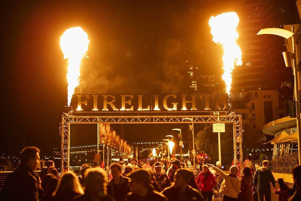 A blazing Firelight sign with jets of flame erupting from the top, as visitors walk below.