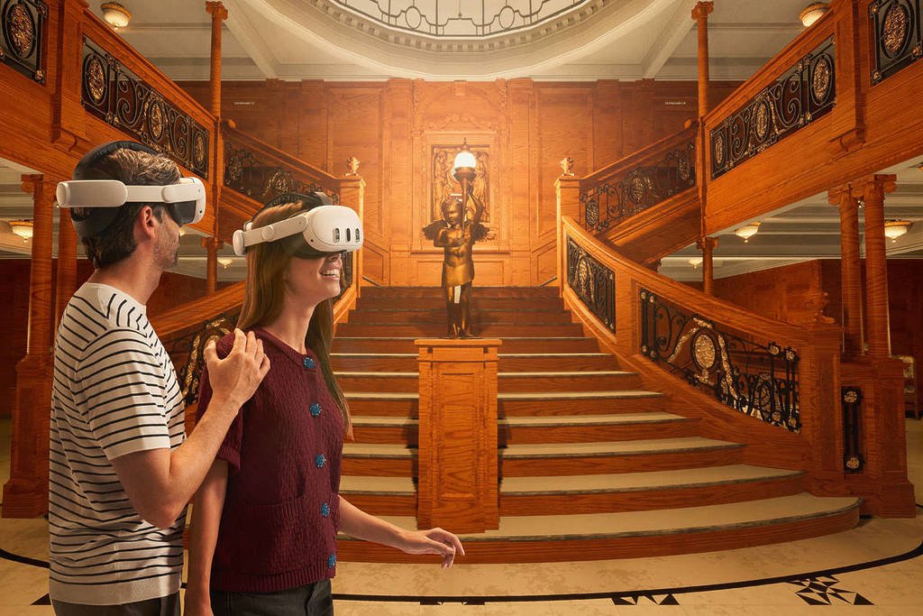 A man and woman wearing VR headsets gaze at the grand entrance stairs of the Titanic.