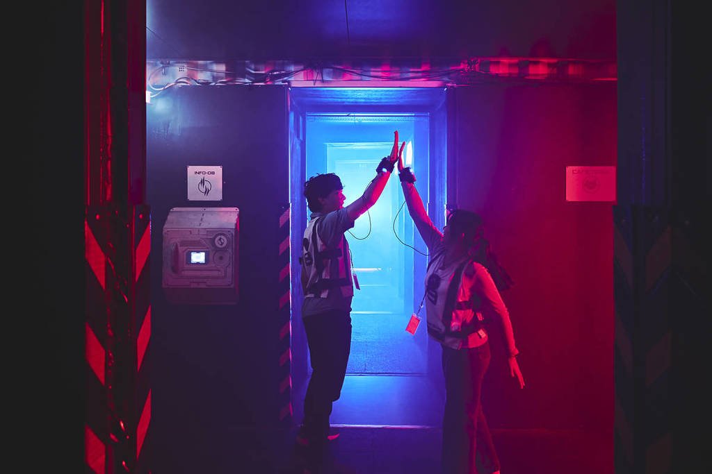 Two players high five inside the Saboteurs. The room is lit with a red light.