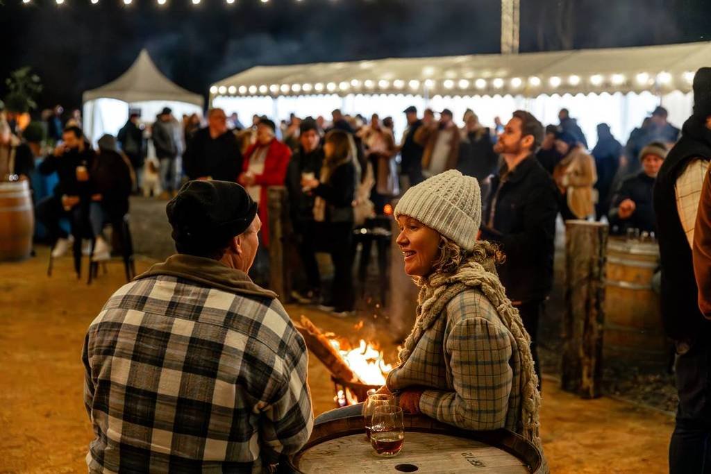 man and woman with wine by a fire at an outdoor market for Fireside Festival